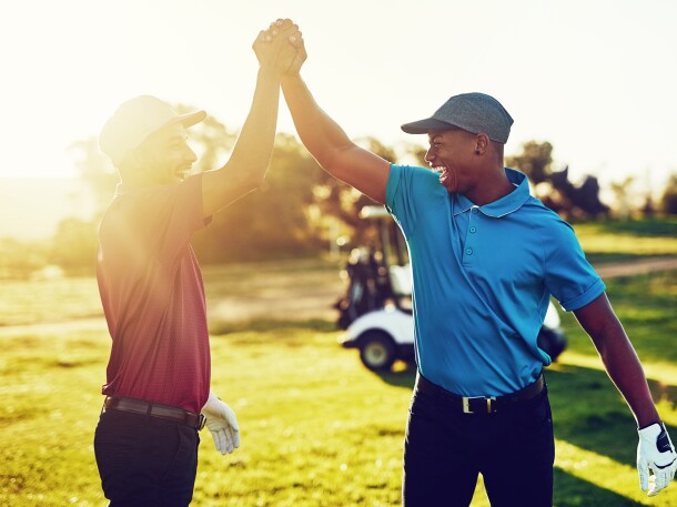 twosome golfers celebrate with high five on golf course with sunshine