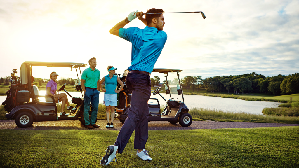 Golfer swinging on golf course with carts and foursome