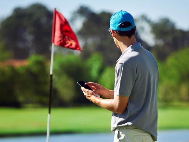 Guy holding mobile device on golf course