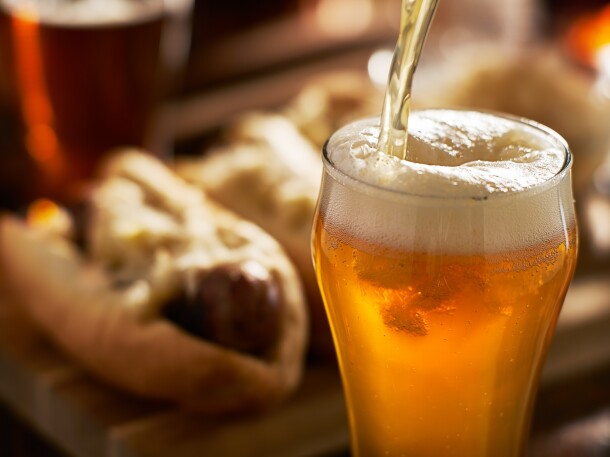 pouring amber beer into mug with bratwursts in background