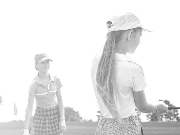 two junior girls - golfers practicing on the course