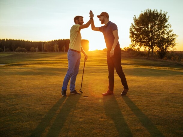 twosome guys on the golf course high fiving at sunset