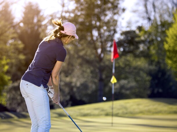 woman chipping onto green of golf course hole