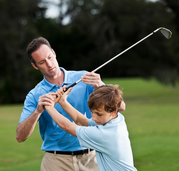 Golf instructor teaching boy (14 years) how to swing golf club, checking grip. Main focus on hands.