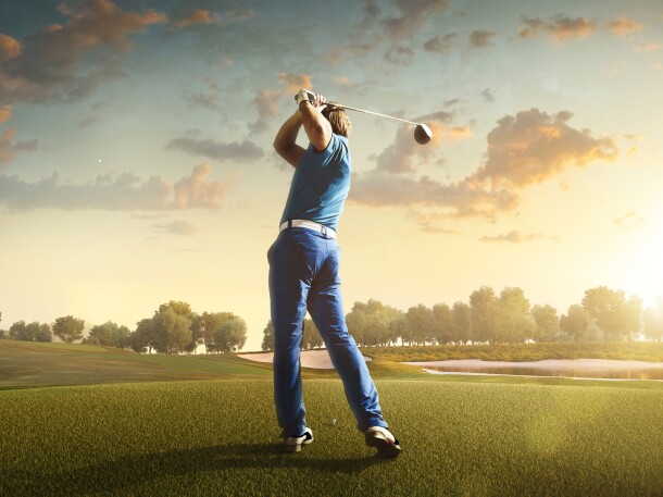 man swinging club on golf course at sunset