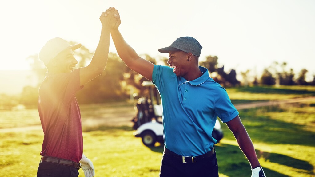 twosome golfers celebrate with high five on golf course with sunshine