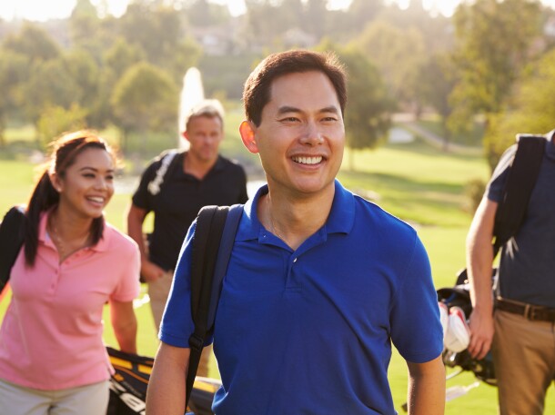 Group Of Golfers Walking Along Fairway Carrying Golf Bags