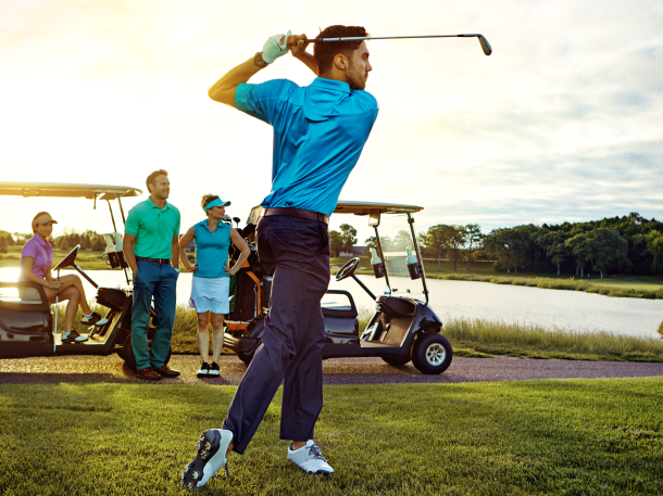 Golfer swinging on golf course with carts and foursome