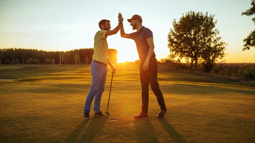 twosome guys on the golf course high fiving at sunset