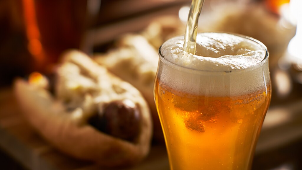 pouring amber beer into mug with bratwursts in background