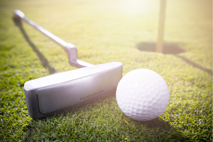 putter on green next to ball and hole