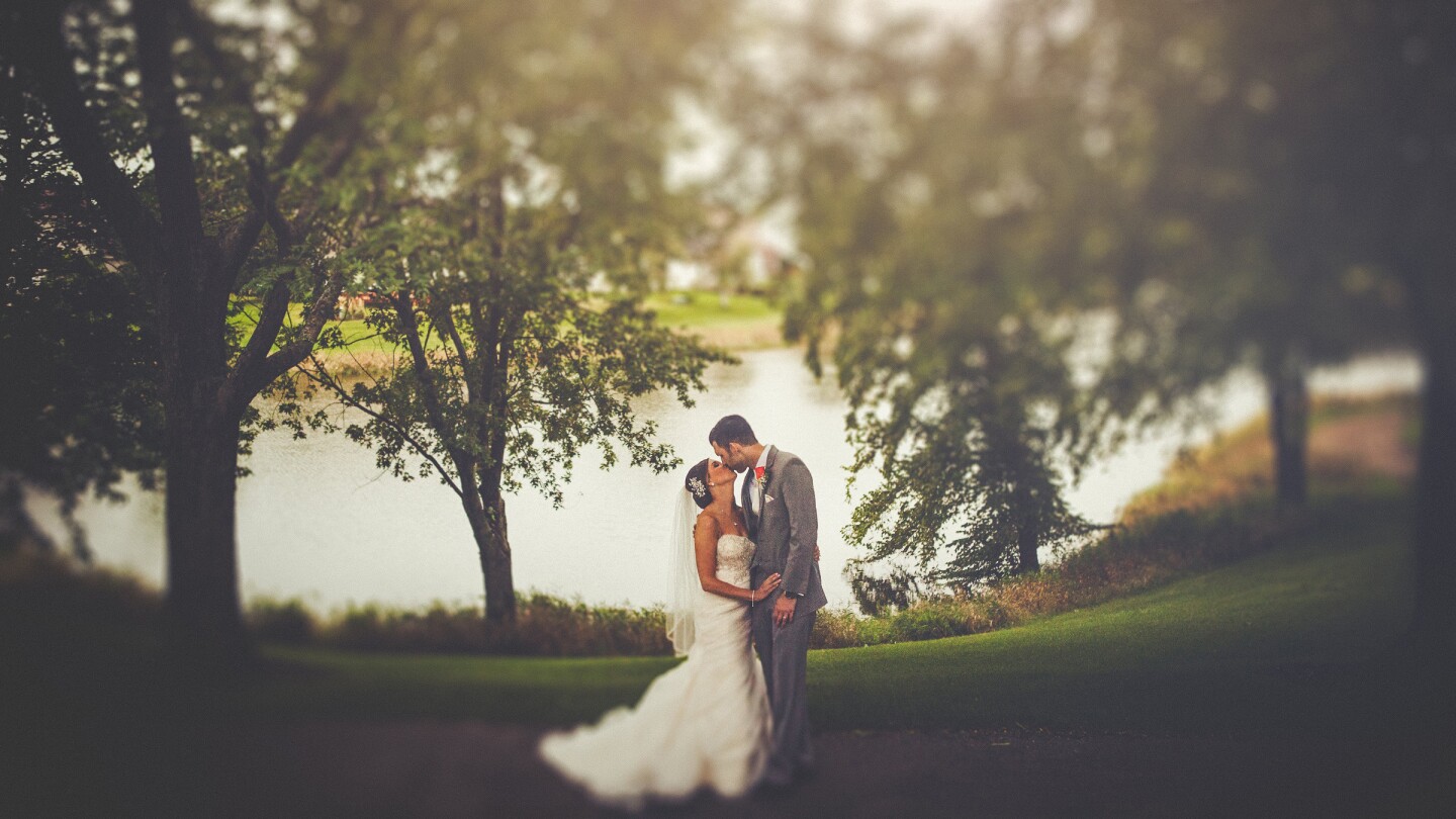 bride and groom kissing under giant tree by lake