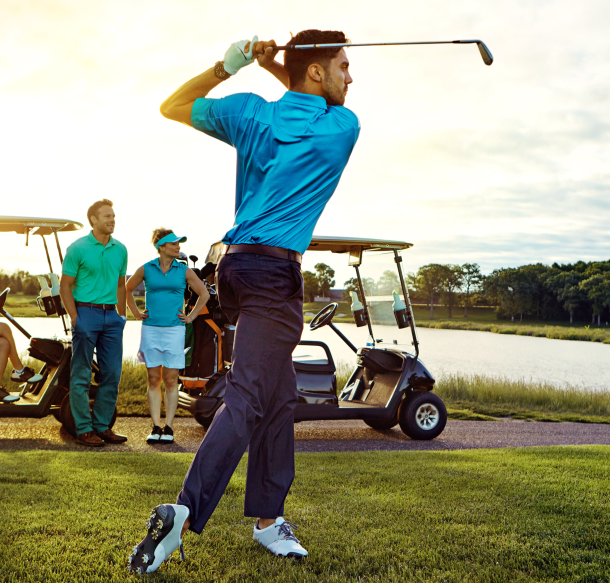 Golfer swinging on golf course with carts and foursome