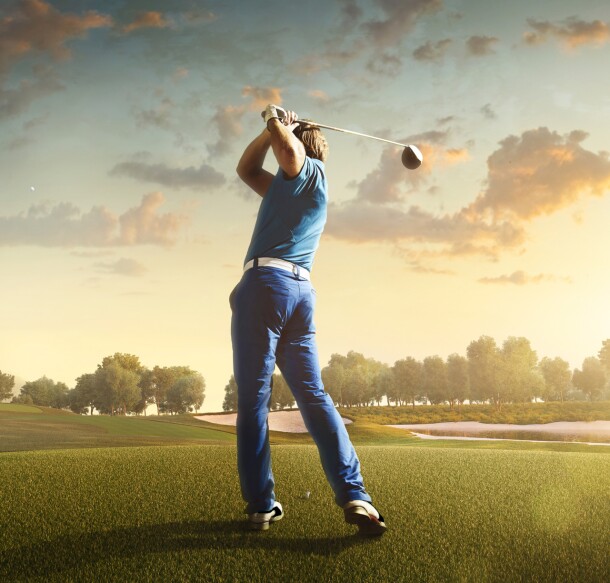 man swinging club on golf course at sunset